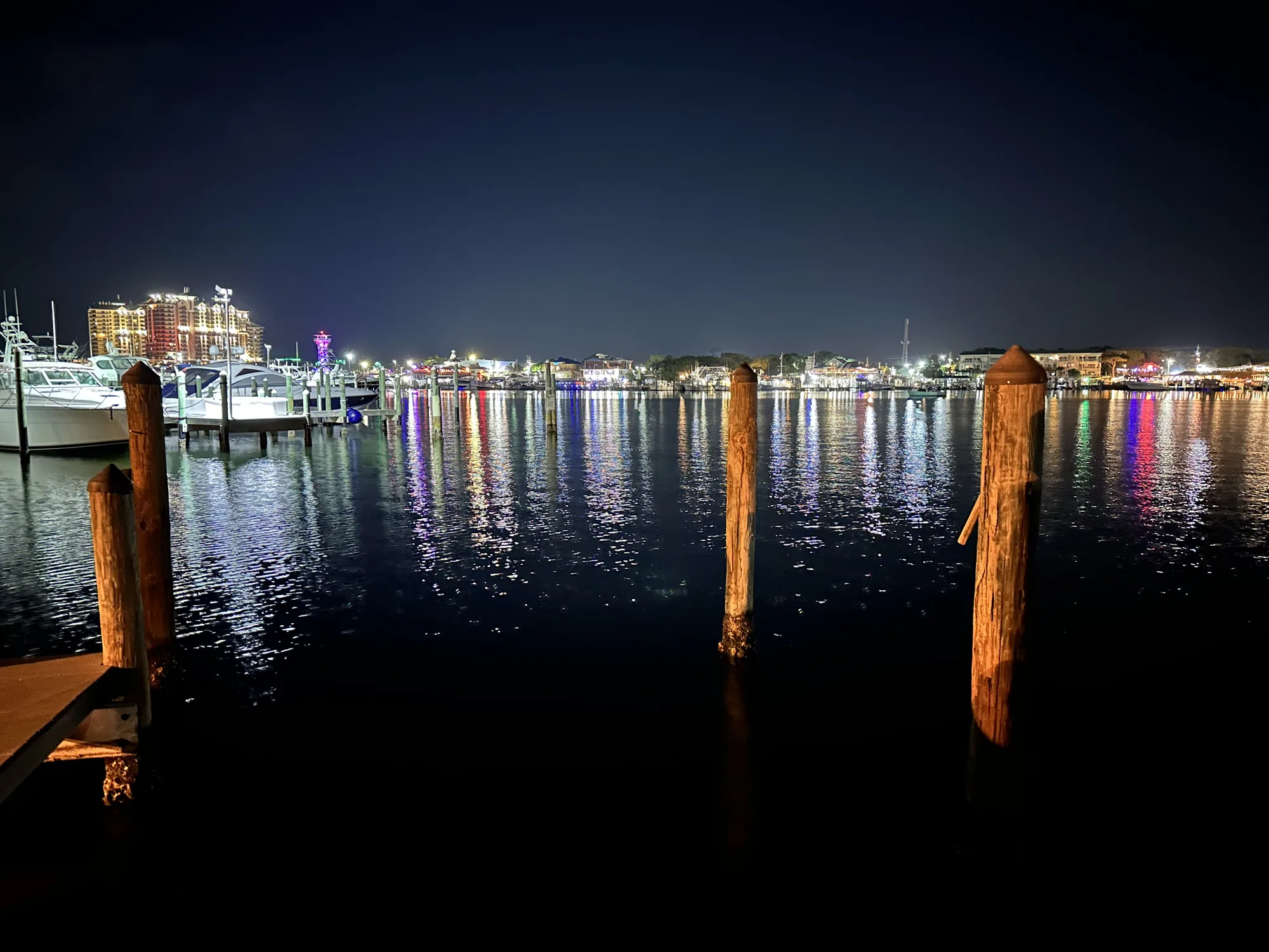 Destin Harbor at night with boats, waterfront lights and reflections.